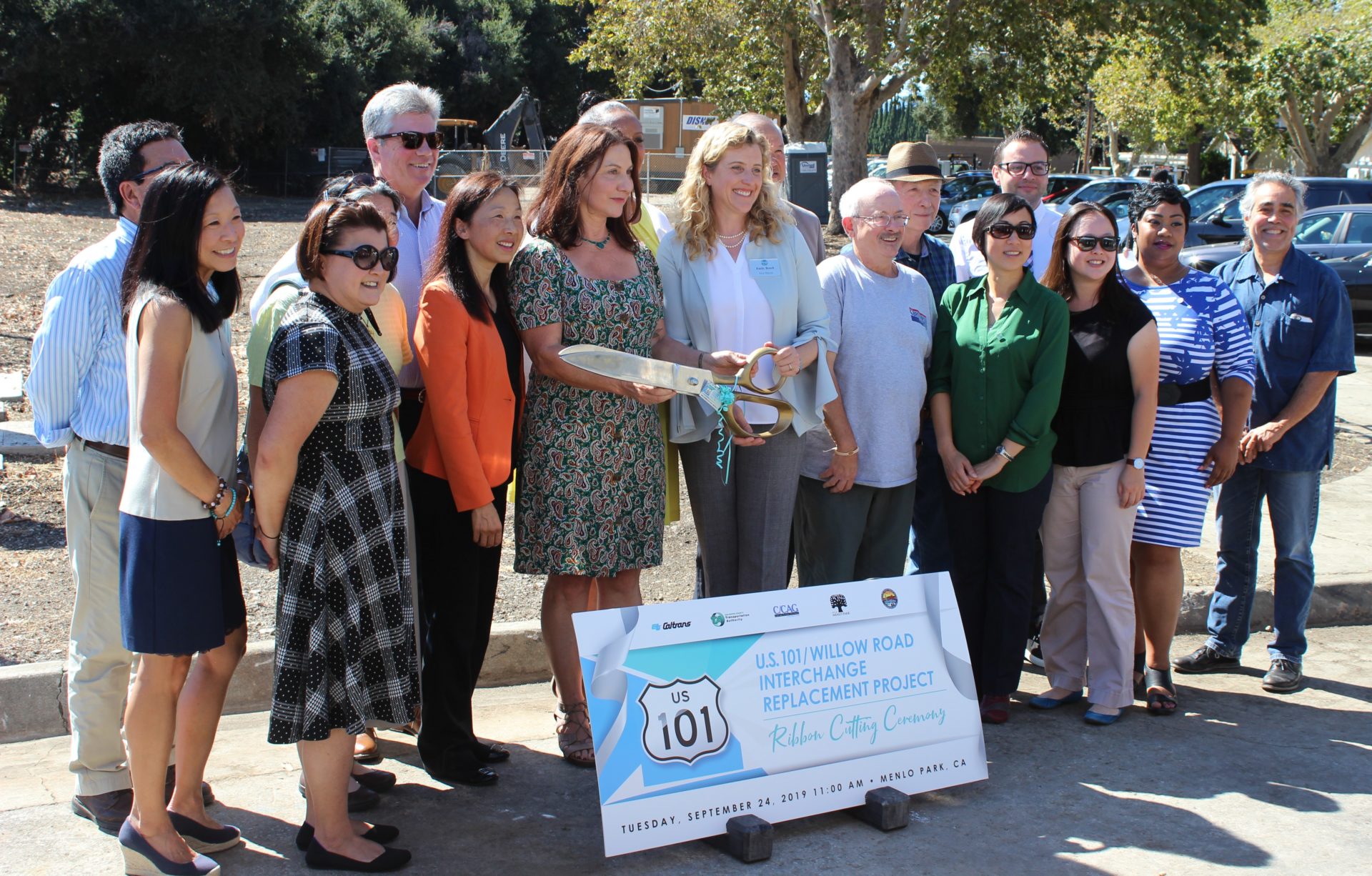 Group of people holding large ribbon cutting scissors at the U.S. 101/Willow Road Interchange Replacement Ceremony